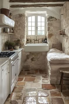 a kitchen with stone walls and flooring next to a sink, stove top oven and window