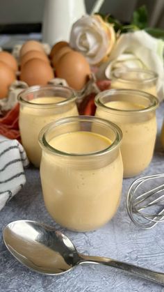 three jars filled with pudding sitting on top of a table next to eggs and whisks