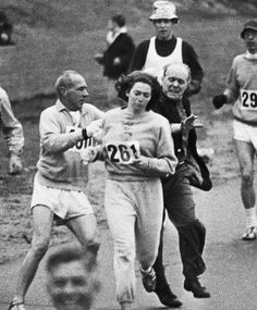 black and white photo of people running in a race with numbers on their shirts as they run