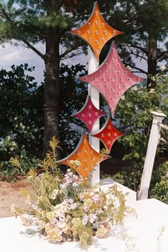 an outdoor decoration with flowers and trees in the background, including three colorful kites