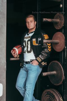 a man standing in front of a metal door holding a football ball and wearing jeans