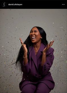 a woman sitting on the ground with her hands in the air and confetti falling around her