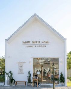 a white brick yard coffee and kitchen building with people sitting at tables outside the front