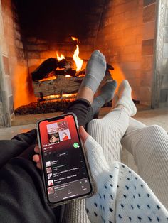 someone is sitting in front of a fireplace with their feet up and holding a cell phone