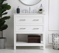 a white bathroom vanity with a round mirror on the wall above it and a potted plant next to it