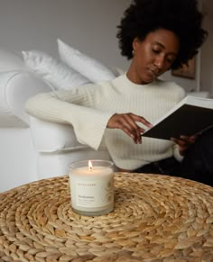 a woman reading a book while sitting on a wicker table with a candle in front of her