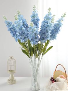 blue flowers are in a vase next to a birdcage and an empty basket