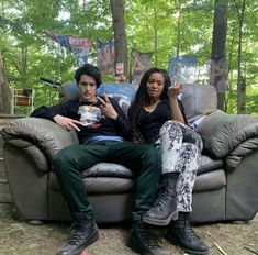 two people are sitting on a couch in the woods, one is pointing at something