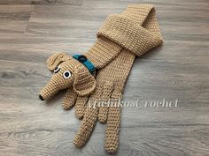 a crocheted dog wearing a scarf on top of a wooden floor next to a pair of gloves