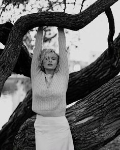 black and white photograph of a woman holding her hands up in the air while standing next to a tree