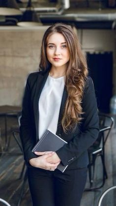 a woman in a suit holding a notebook and standing next to some tables with chairs