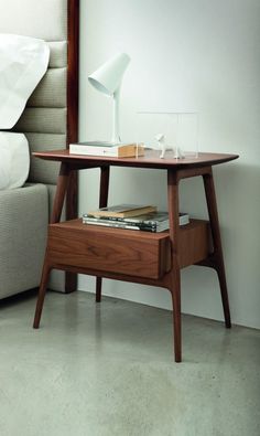 a small wooden table with a lamp on it next to a bed and a mirror