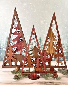 three wooden christmas trees with snowflakes on them and pine cones in the foreground