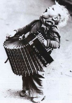 an old black and white photo of a little boy with accordions in his hands