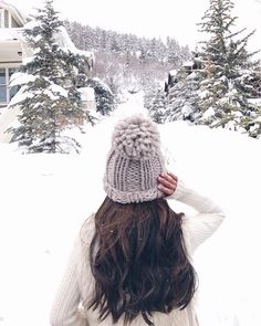 a woman standing in the snow with her back to the camera, wearing a knitted hat