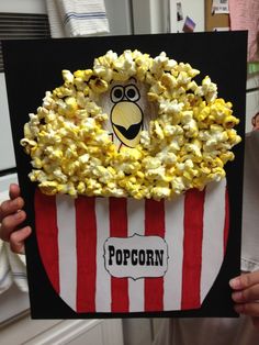 a person holding up a popcorn bag with the word popcorn on it in front of them