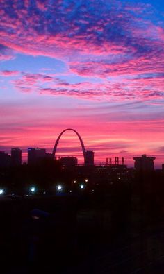 the st louis skyline is silhouetted against a pink and blue sky