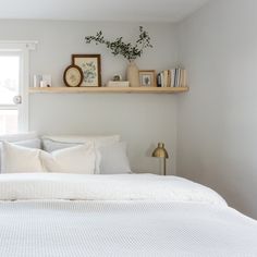 a bed with white linens and pillows in a small room next to a window