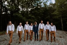 a group of men standing next to each other on top of a gravel road in front of trees