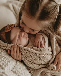 a woman holding a baby in her arms while laying on top of a white blanket