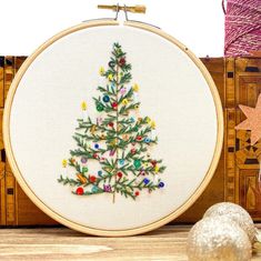 a cross stitch christmas tree on a wooden table next to some other ornaments and decorations