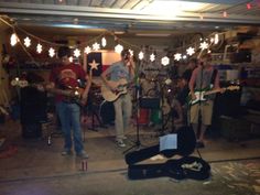 a group of people that are playing guitars in a room with lights strung from the ceiling