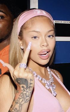 a woman in pink shirt pointing at the camera with finger on her lips and another person behind her