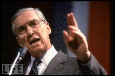 a man in suit and tie giving a speech with his hands out to the side