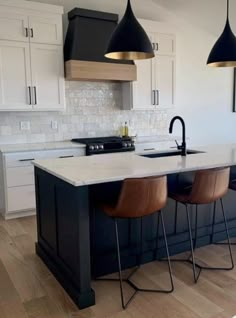 a kitchen island with three stools in front of it and two pendant lights hanging from the ceiling