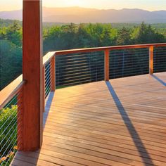 a wooden deck with metal railings overlooking the trees and mountains in the distance at sunset