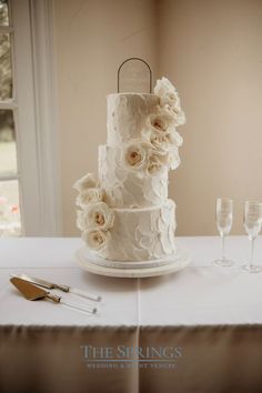 a three tiered wedding cake with white flowers on the top and two champagne flutes