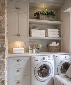 a washer and dryer in a small room with stone walls, white cabinets and open shelving