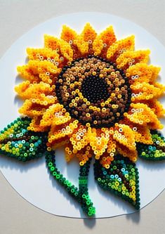 a sunflower made out of plastic beads on a white plate with green and yellow beading