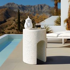 a table with a vase on it next to a pool and mountains in the background