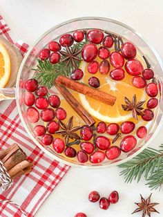 a bowl filled with orange slices, cinnamon sticks and cranberries on top of a red checkered table cloth