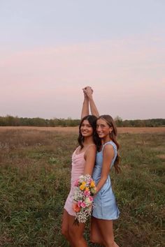 two young women standing next to each other in a field with their arms raised up