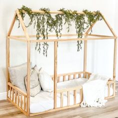 a baby crib with plants growing over it's roof and pillows on the floor