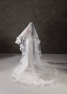 a white veil with flowers on it is sitting in front of a concrete wall and floor