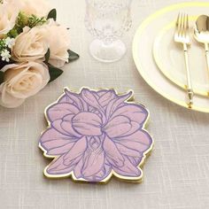 a pink flower sitting on top of a table next to a white plate and silverware