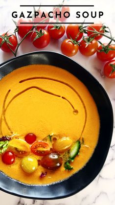 a bowl of soup with tomatoes and cucumbers on the side next to some cherry tomatoes