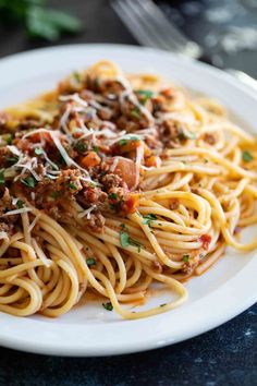 a plate of spaghetti with meat and parmesan cheese on the top is ready to be eaten