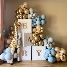 a giraffe standing in front of a tall stack of balloons and letter blocks