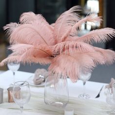 there is a vase with some pink feathers on it and wine glasses next to it