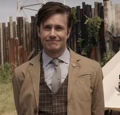 a man wearing a suit and tie standing in front of a wooden fenced area