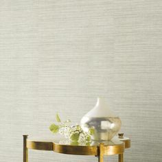 a white vase sitting on top of a gold table next to a wallpapered wall