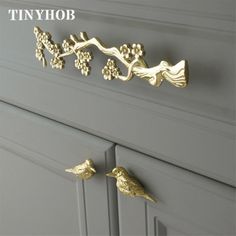 two gold birds are on the handles of a gray dresser