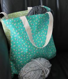 two balls of yarn sit next to a green bag on a black leather chair with a white handle