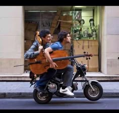 two men riding on the back of a motorcycle with an instrument strapped to it's back