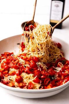 a white bowl filled with spaghetti and tomatoes next to a bottle of wine on a table