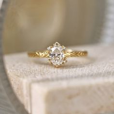 a yellow gold engagement ring with an oval diamond in the center on a white surface